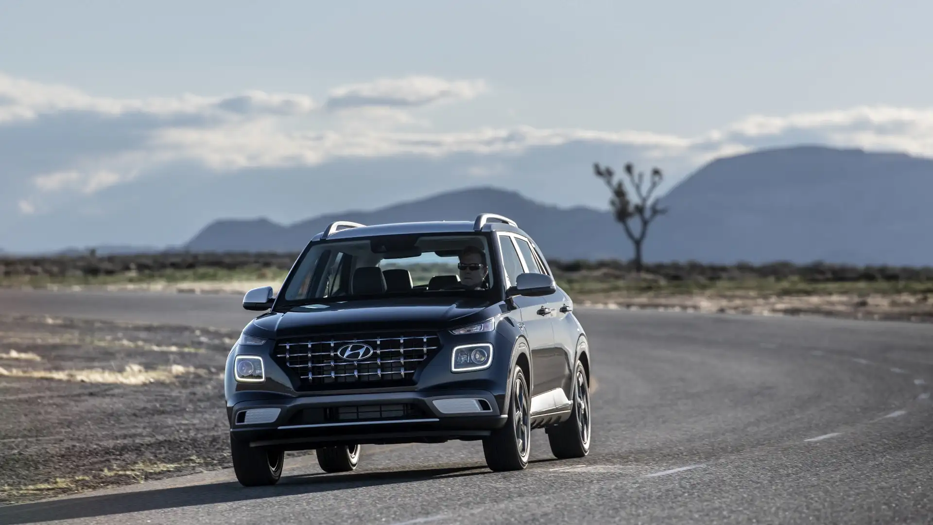2026 Hyundai Venue SUV driving on an open road with dark exterior color, signature grille, and compact crossover design.