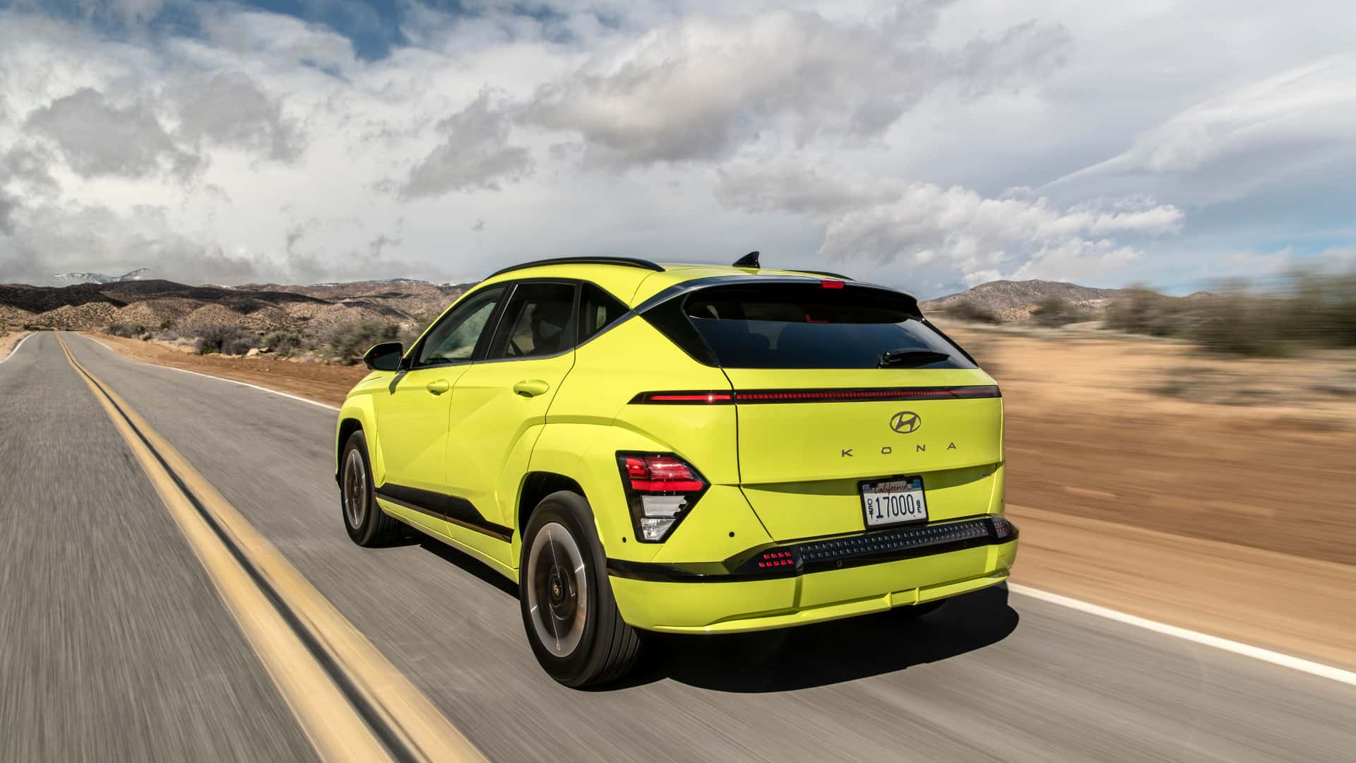 Rear three-quarter view of a lime green 2025 Hyundai Kona Electric driving on an open road.