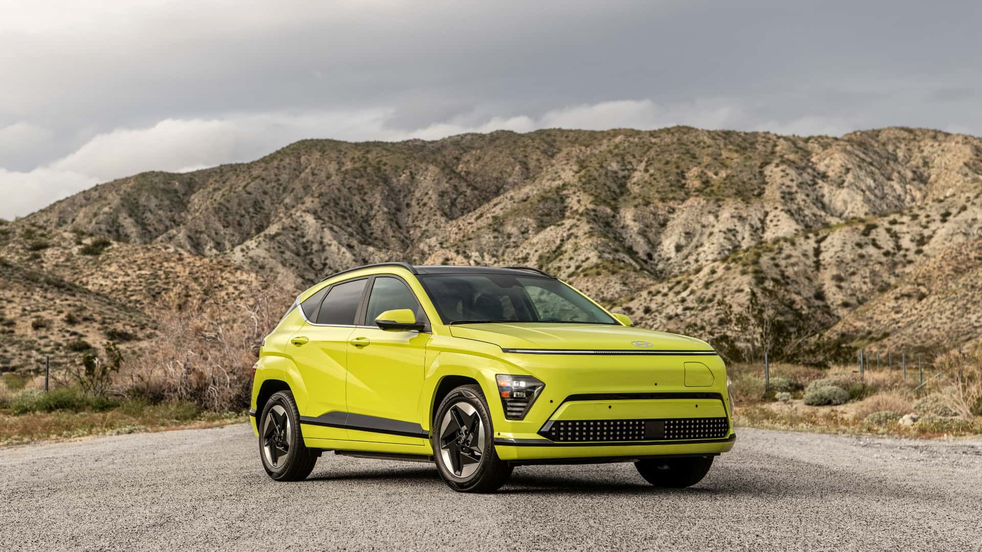 2025 Hyundai Kona Electric lime green electric SUV parked on gravel with rocky mountains in the background.