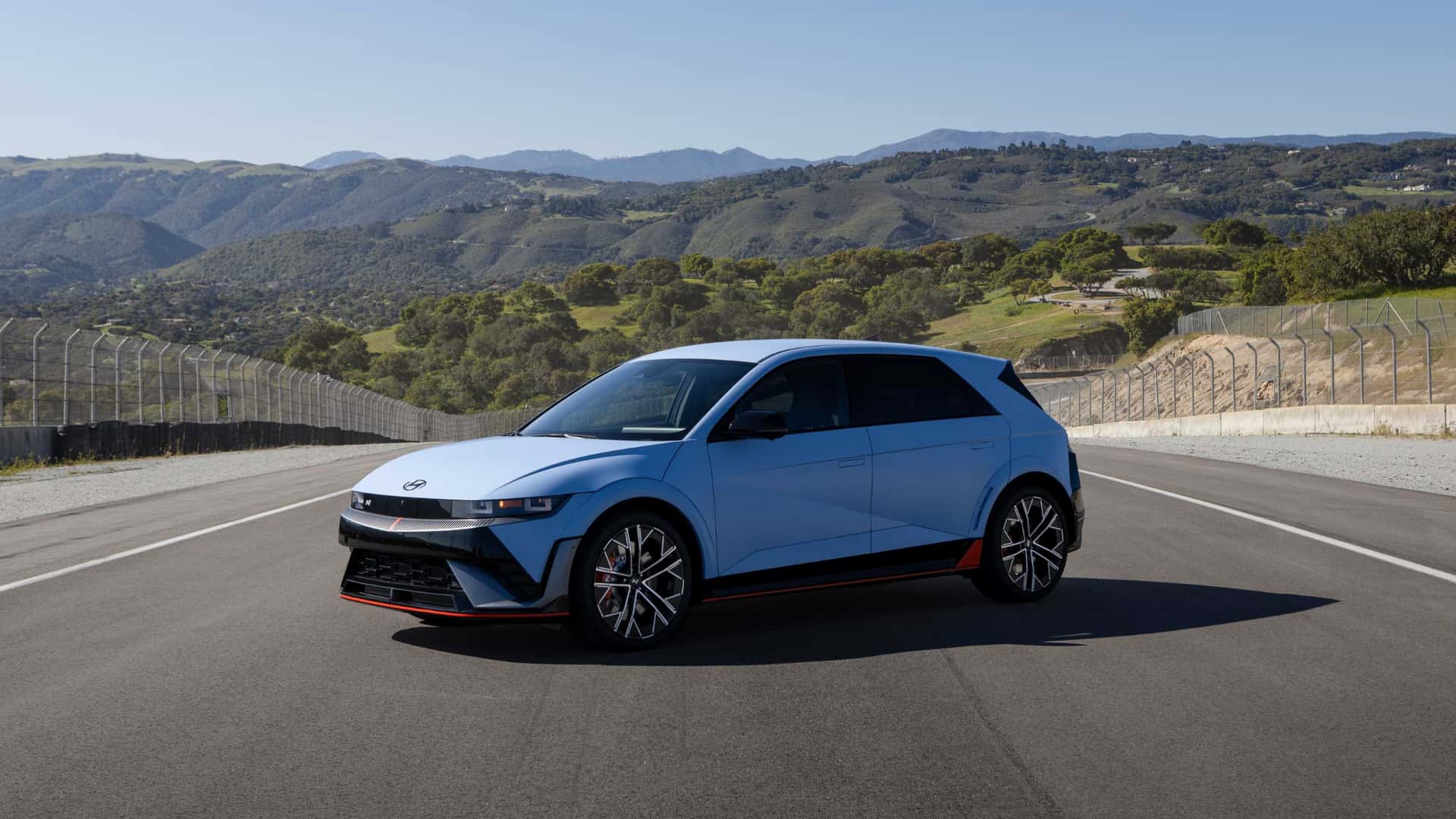 2026 Hyundai IONIQ 5 N blue performance EV parked on a racetrack with hills and fencing in the distance.