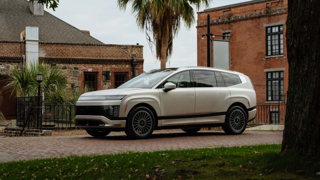 2026 Hyundai IONIQ 9 white exterior parked on brick street with modern urban background, showing side profile and sleek design.