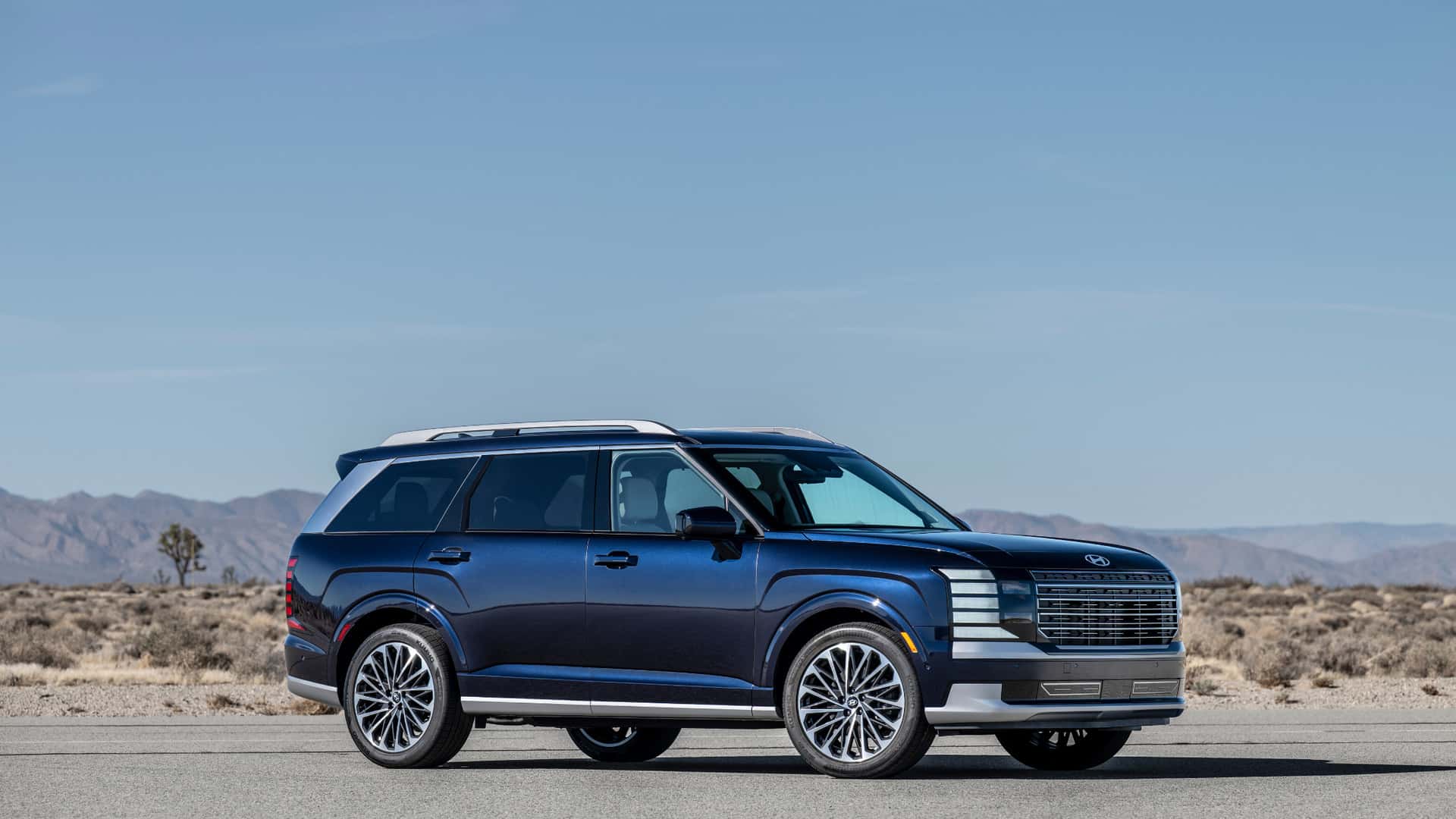 Blue 2026 Hyundai Palisade SUV parked on desert road with mountain backdrop.