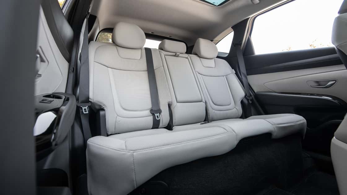 2026 Hyundai Tucson Hybrid interior rear view highlighting second-row seating, spacious cabin, and light-colored upholstery.
