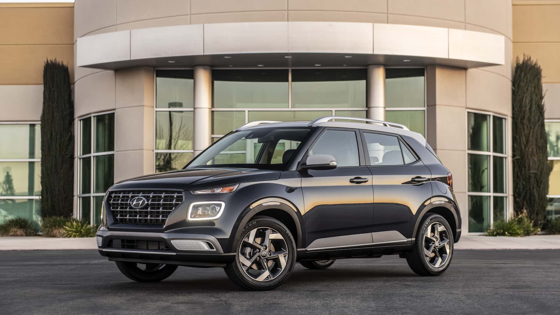 2026 Hyundai Venue subcompact SUV in dark gray parked in front of modern building.