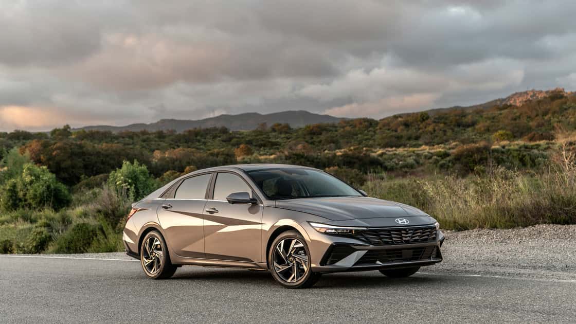 2026 Hyundai Elantra sedan in bronze parked on a scenic road with mountain views and dramatic cloudy sky.