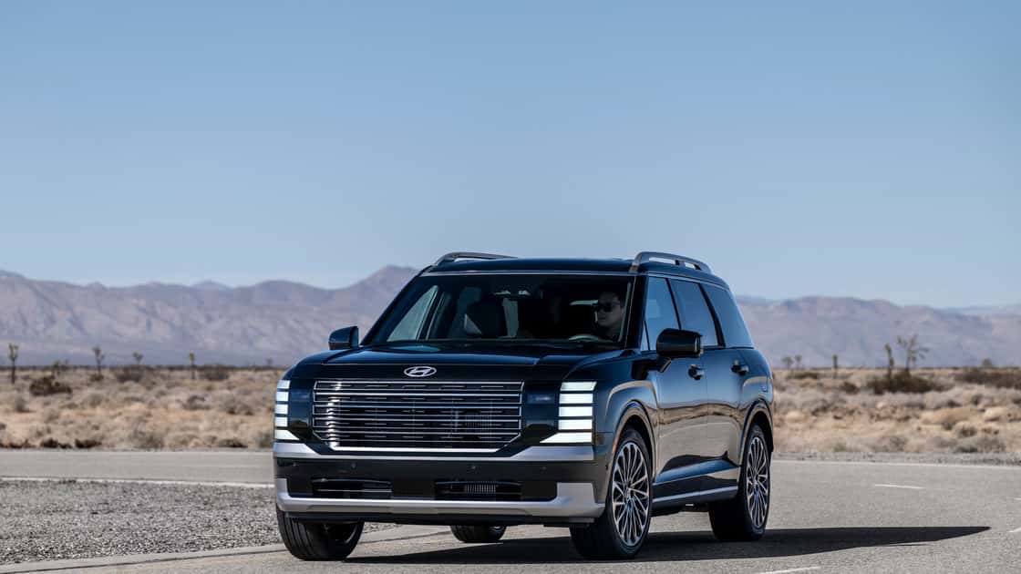 2026 Hyundai Palisade in black driving on a desert road with bold front grille, LED lighting, and mountain backdrop.
