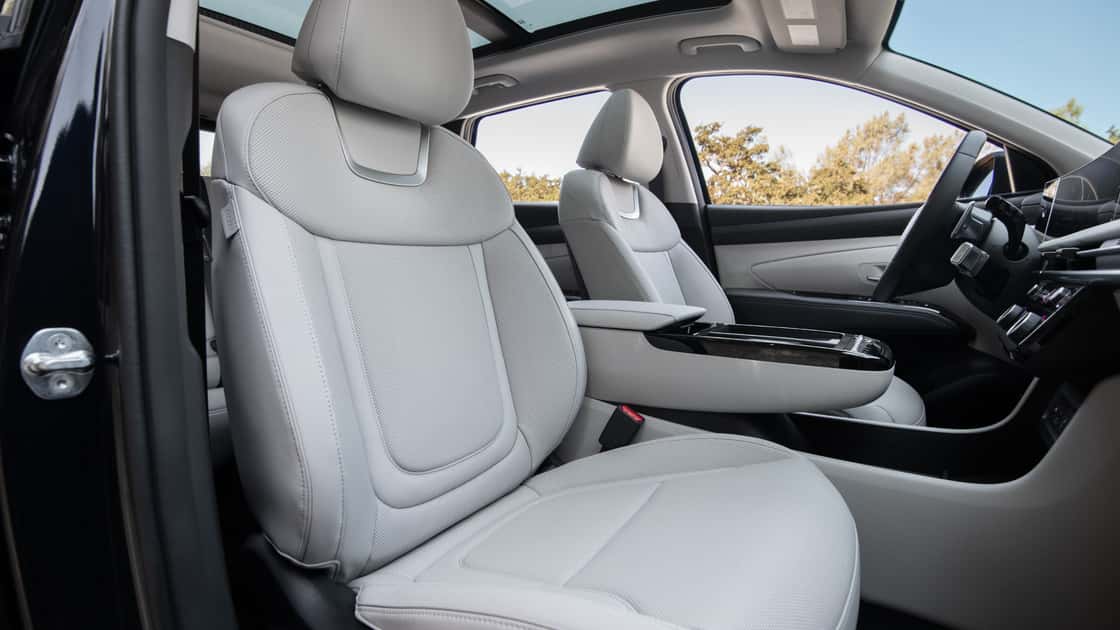 2026 Hyundai Tucson Hybrid front seats with light upholstery, panoramic roof, and modern center console.