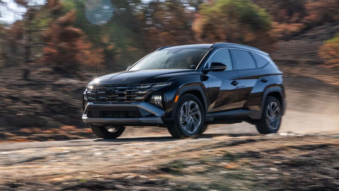 2026 Hyundai Tucson Hybrid in black driving on a dirt road with rugged SUV styling and outdoor capability.