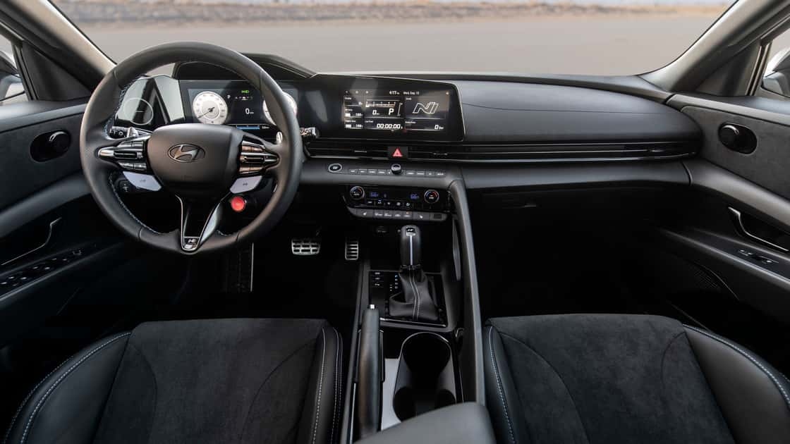 2026 Hyundai Elantra N interior with sport steering wheel, performance display, manual shifter, and black cabin trim.