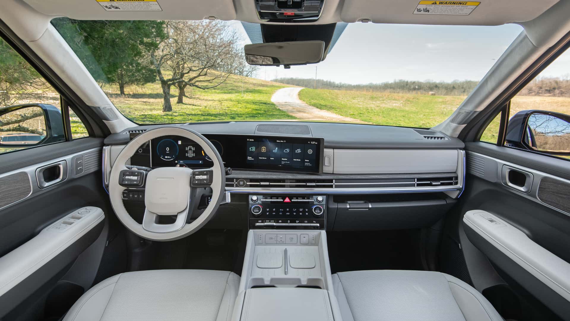 2026 Hyundai Santa Fe interior with wide digital display, light cabin trim, dual climate controls, and open road view.