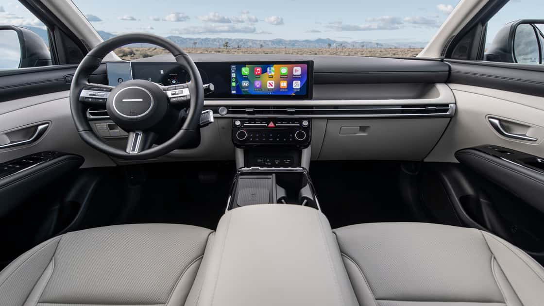 2026 Hyundai Tucson interior with wide digital display, light cabin trim, steering wheel, and touchscreen controls.