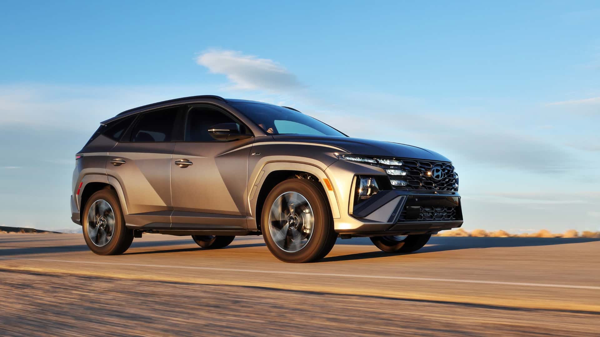 2026 Hyundai Tucson in bronze driving at sunset with sharp body lines, black trim, and compact SUV styling.