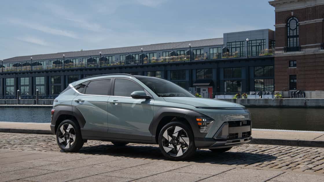 2027 Hyundai Kona gray compact SUV parked on a waterfront street with angular body lines and modern alloy wheels.