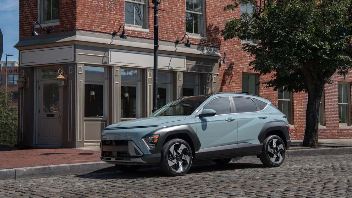 2027 Hyundai Kona compact SUV parked on a cobblestone street beside a brick building.