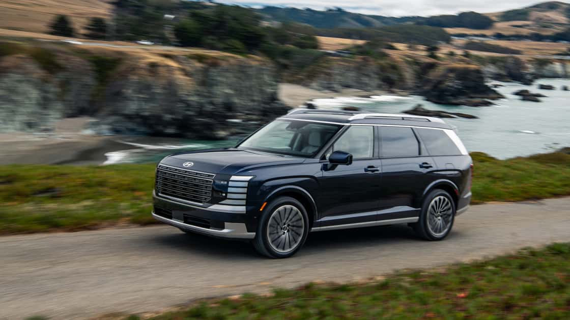 2027 Hyundai Palisade black SUV driving along a coastal road with premium styling, large grille, and three-row family design.