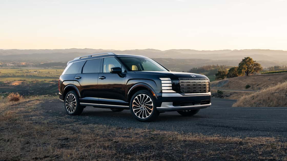 2027 Hyundai Palisade black SUV parked on a scenic hillside road during sunset.