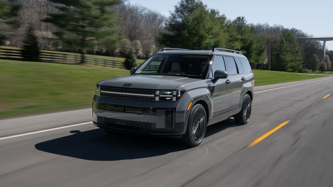 2027 Hyundai Santa Fe gray SUV driving on a paved road with trees and motion blur in the background.