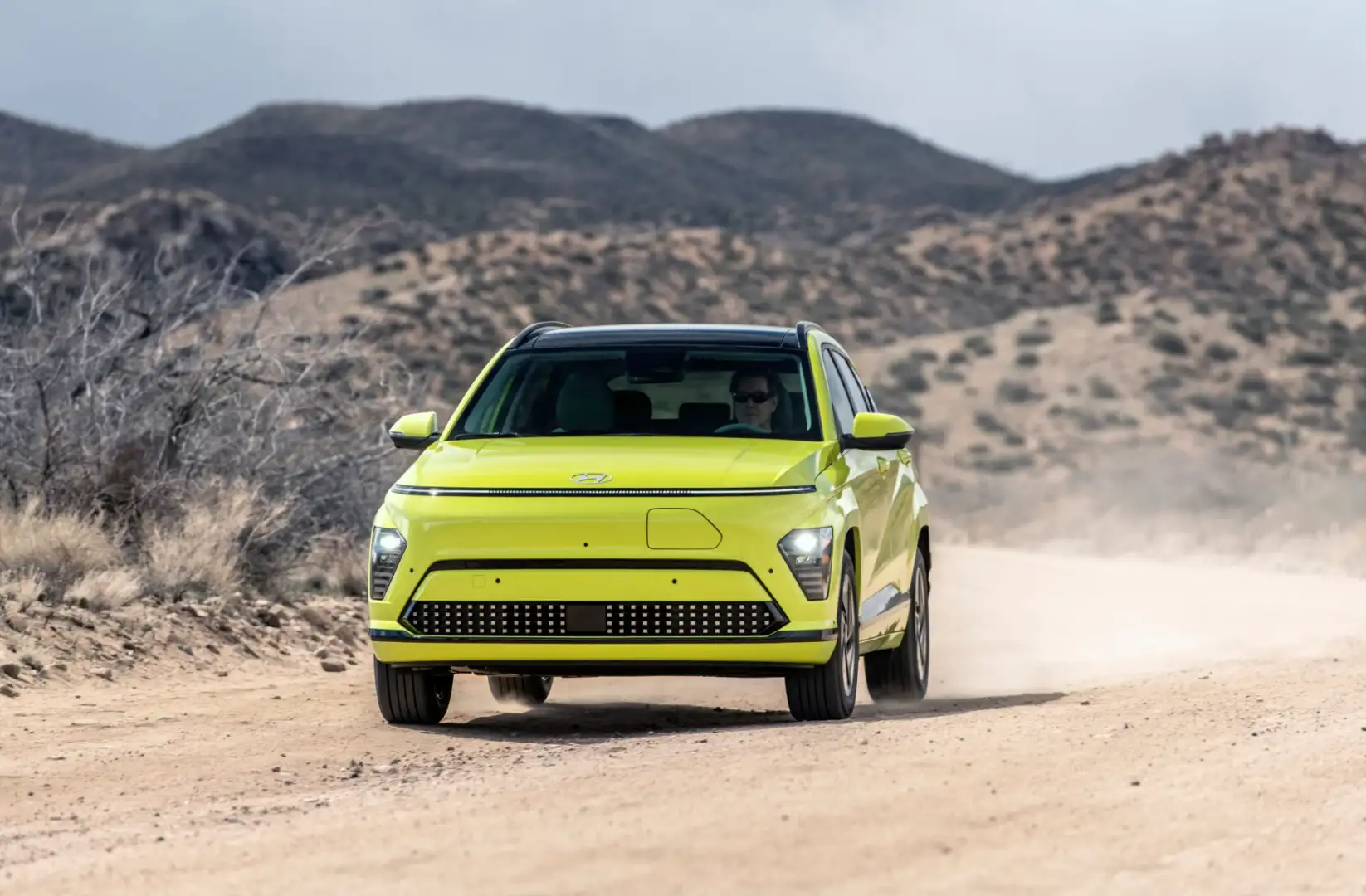 A vibrant yellow 2025 Hyundai Kona Electric driving on a dusty road.