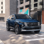 A blue 2025 Hyundai Tucson parked on an urban street with modern buildings.