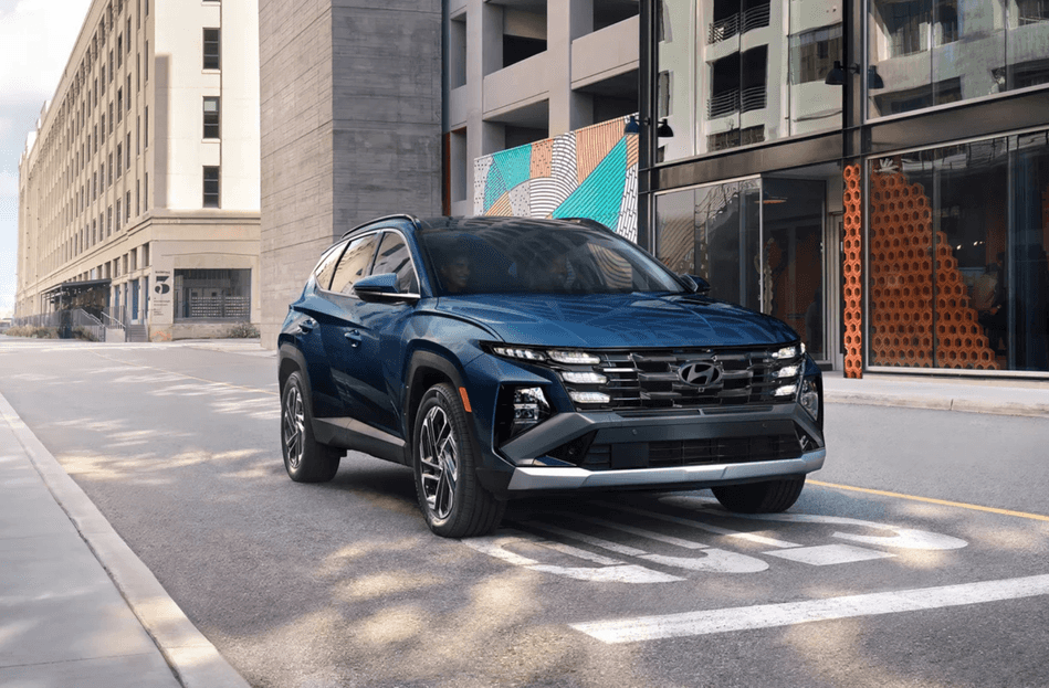 A blue 2025 Hyundai Tucson parked on an urban street with modern buildings.