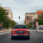 A red 2025 Hyundai Venue driving through a city street with blurred motion.