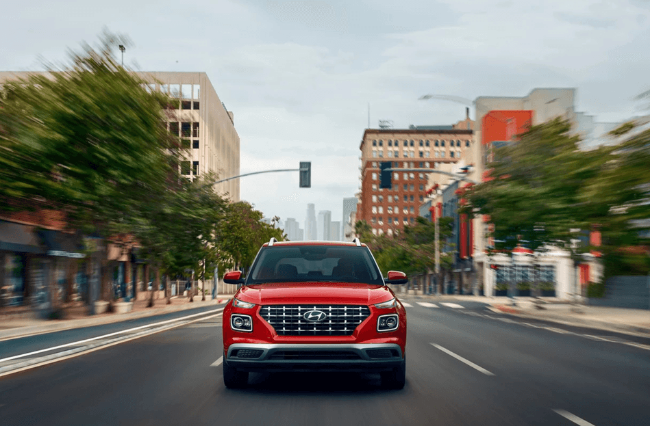 A red 2025 Hyundai Venue driving through a city street with blurred motion.