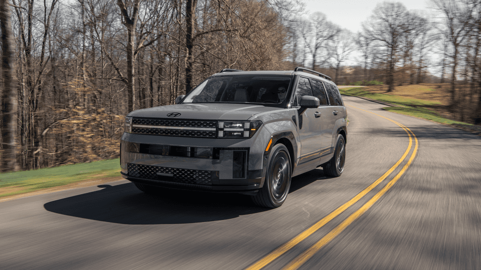 A gray 2025 Hyundai Santa Fe SUV on a scenic road with blurred trees in the background.