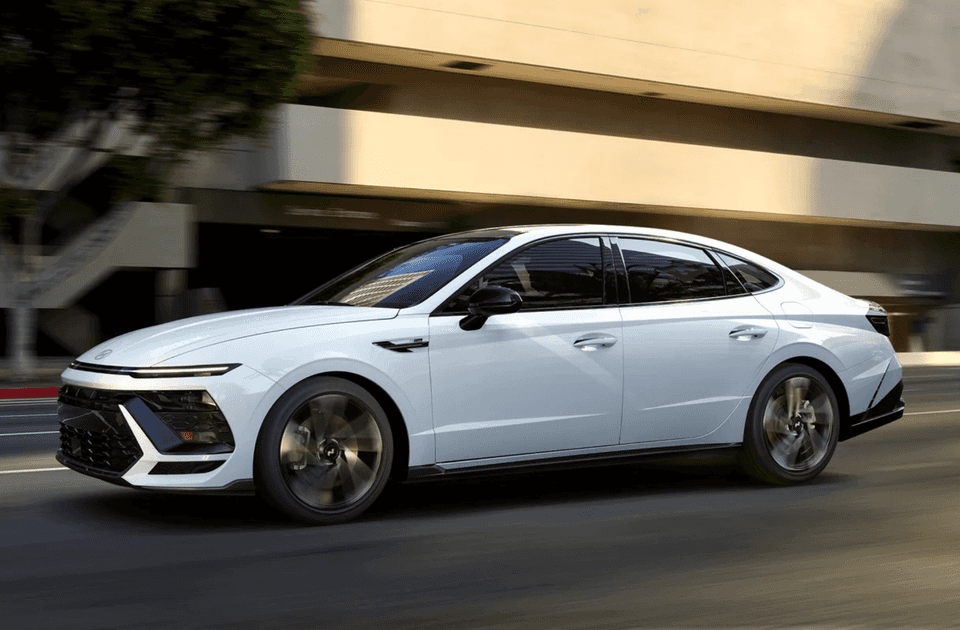 White 2025 Hyundai Sonata sedan driving in city with blurred background for motion effect.