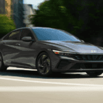 2025 Hyundai Elantra Hybrid in dark gray driving through an urban street with blurred city background.
