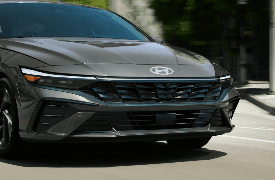Front view close-up of the 2025 Hyundai Elantra Hybrid showcasing its bold grille, sleek headlights, and modern aerodynamic lines while in motion.