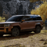 2025 Hyundai Santa Fe Hybrid in bronze parked near a forest as a family plays nearby during fall.