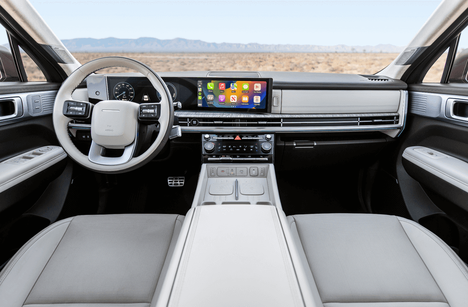 Interior of the 2025 Hyundai Santa Fe Hybrid showcasing a modern digital dashboard with dual screens, Apple CarPlay, and a spacious front cabin with light leather seating.