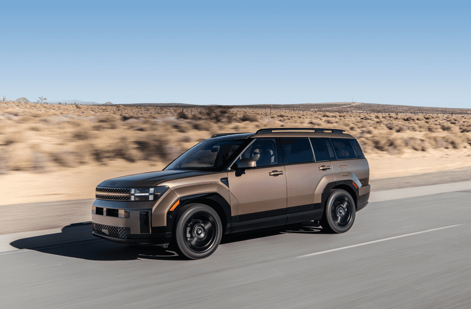 2025 Hyundai Santa Fe Hybrid in motion on a desert highway, featuring a rugged design and bronze finish under a clear blue sky.