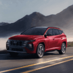 2025 Hyundai Tucson Hybrid in red driving along a mountain road with fog and rugged peaks in the background.