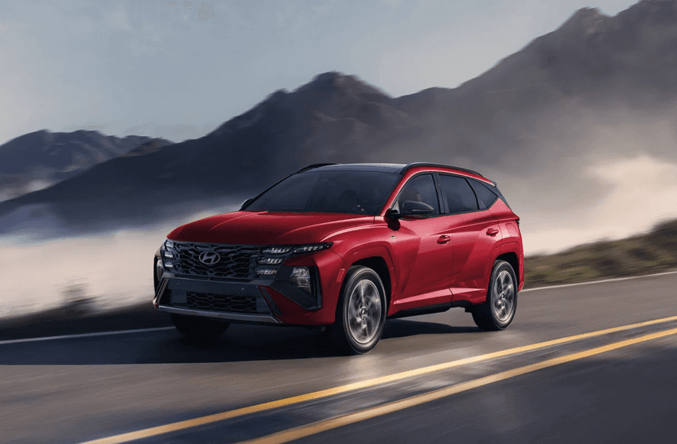 2025 Hyundai Tucson Hybrid in red driving along a mountain road with fog and rugged peaks in the background.