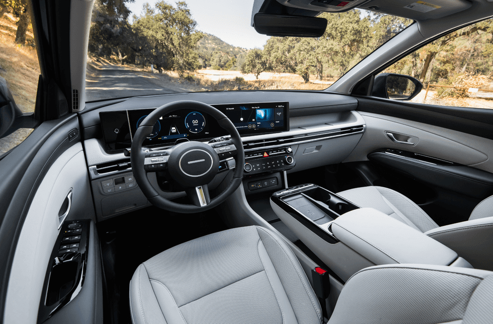 Interior view of the 2025 Hyundai Tucson Hybrid featuring a fully digital instrument cluster, wide infotainment display, and a sleek, modern dashboard design in a two-tone color scheme.