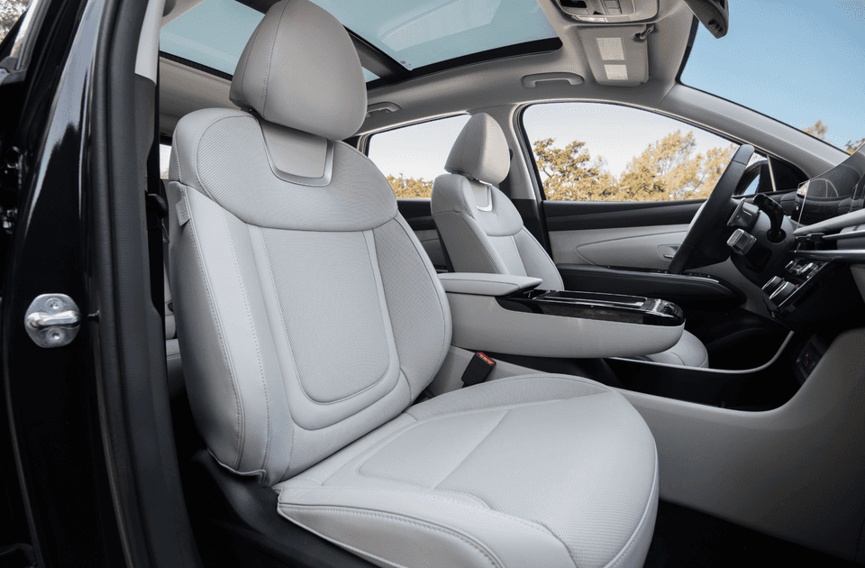Side view of the 2025 Hyundai Tucson Hybrid’s front seats with light leather upholstery, panoramic sunroof, and minimalist interior styling.