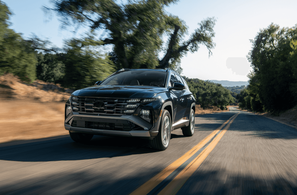2025 Hyundai Tucson Hybrid driving on a scenic rural road, showcasing its bold front grille and LED headlights under natural daylight.