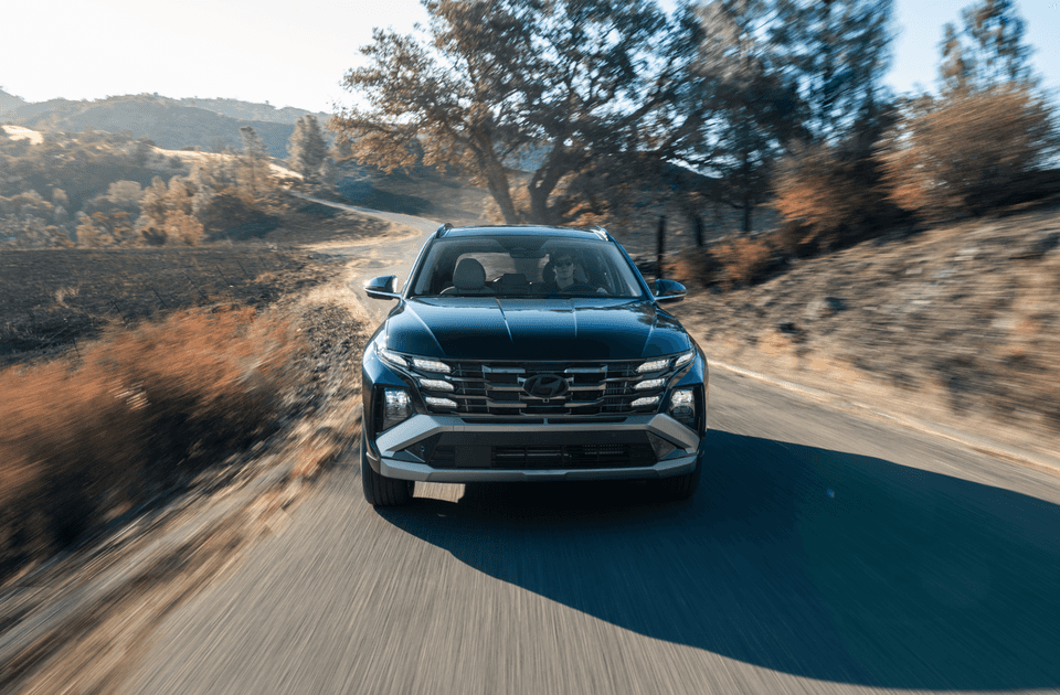 2025 Hyundai Tucson Hybrid driving on a scenic forest road with autumn colors in the background.