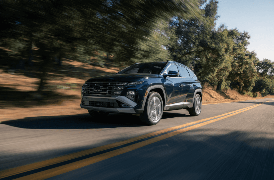 2025 Hyundai Tucson Hybrid driving on a tree-lined road with modern LED lighting and sleek design.