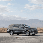 2025 Hyundai Palisade SUV driving on open desert highway with mountain backdrop and chrome-accented exterior.