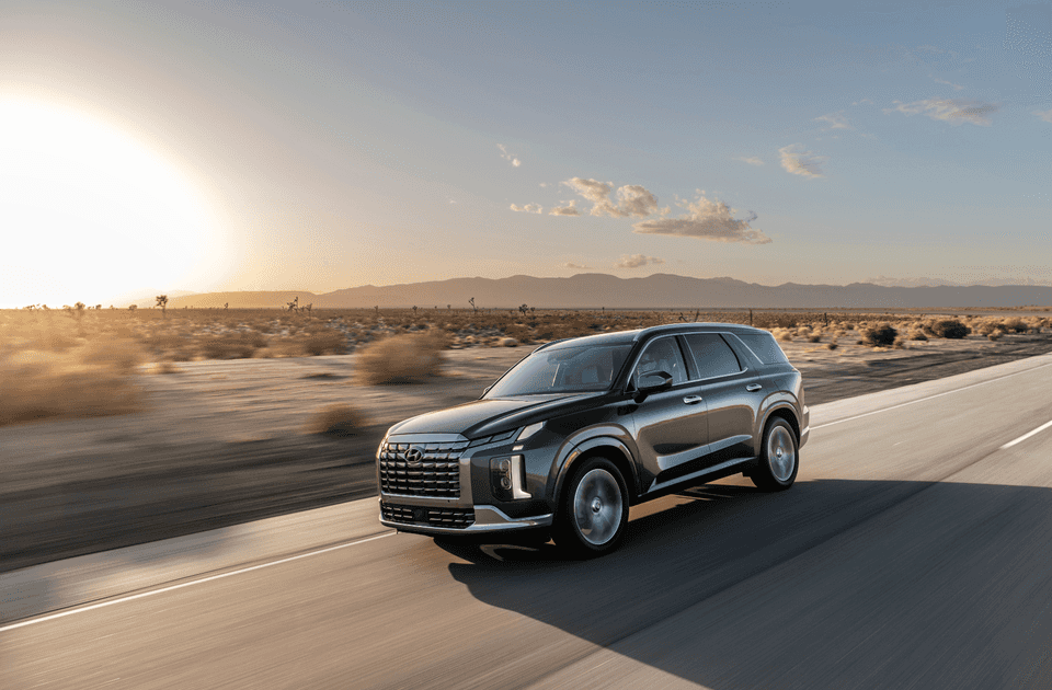 2025 Hyundai Palisade exterior in motion on open highway at sunset with desert landscape background.