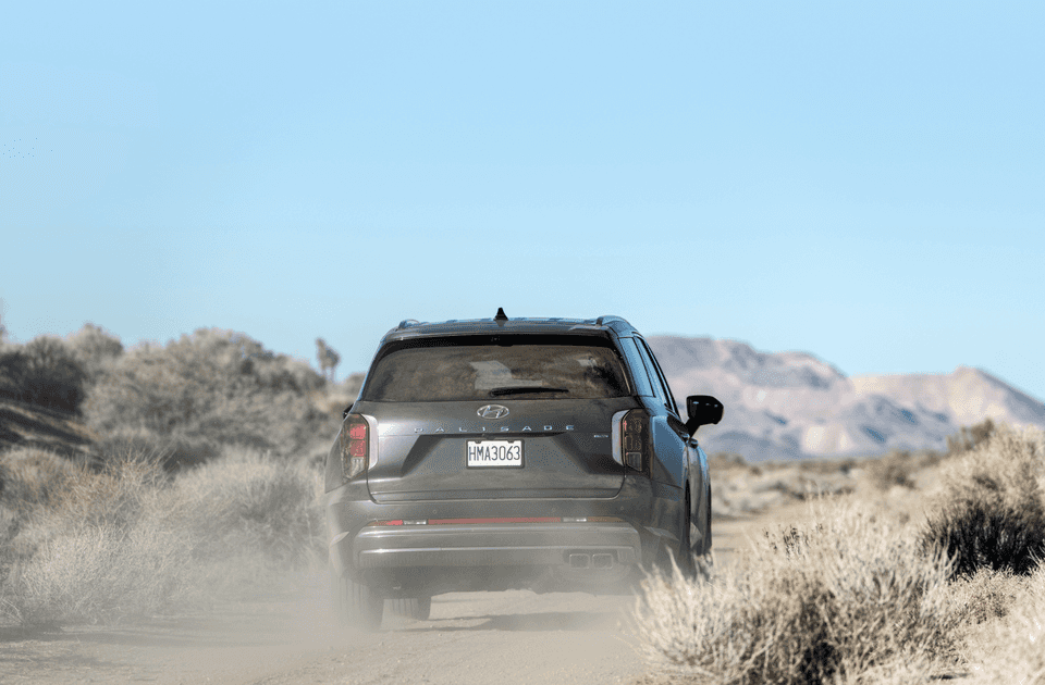 2025 Hyundai Palisade rear profile driving through dusty desert terrain with mountain backdrop.