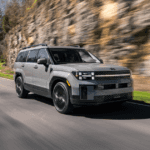 2025 Hyundai Santa Fe SUV in motion on a winding road, featuring boxy profile, LED lights, and matte gray finish.