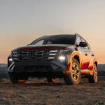 Front view of the 2025 Hyundai Tucson SUV parked on rugged terrain at sunset, showcasing LED headlights and bold grille design..