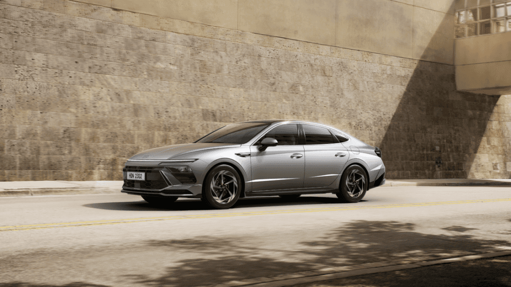 2026 Hyundai Sonata midsize sedan in silver driving past city wall with sharp sporty exterior lines.