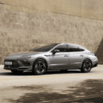 2026 Hyundai Sonata midsize sedan in silver driving past city wall with sharp sporty exterior lines.