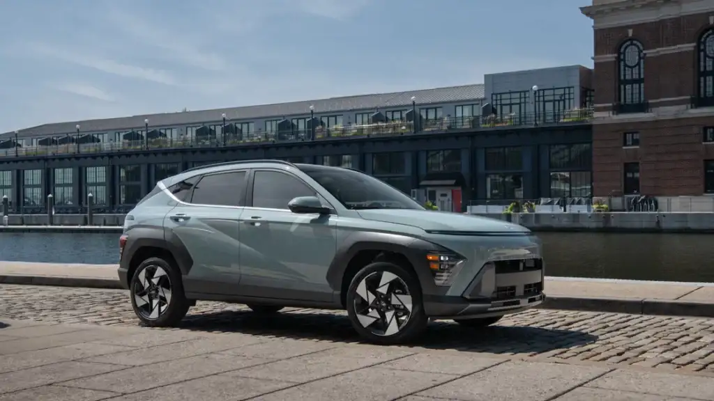 Exterior of 2026 Hyundai Kona in sage green parked near the waterfront with modern architecture behind.