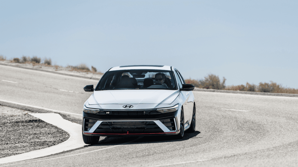 2026 Hyundai Elantra N driving on a curved road showcasing its sporty front design and performance.