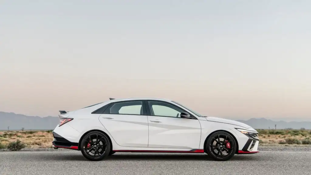 Side profile of a white 2026 Hyundai Elantra N with black wheels and red trim on an open desert road.